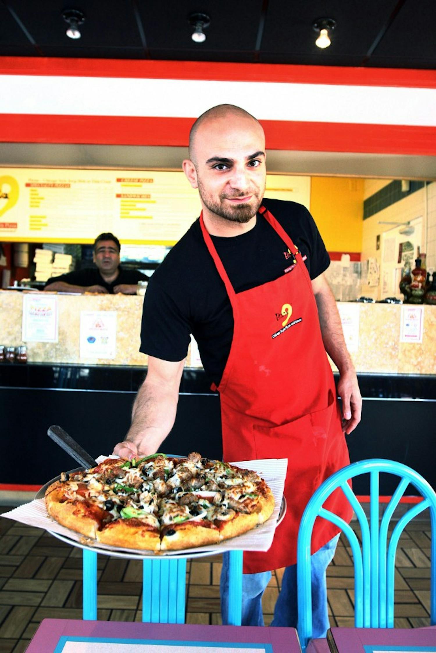 	Co-owners Hass Aslami, left, and Rod Etemadi display a deluxe pizza at Pizza 9’s Gibson location on Monday. Pizza 9 is holding their first annual pizza eating contest on Saturday.