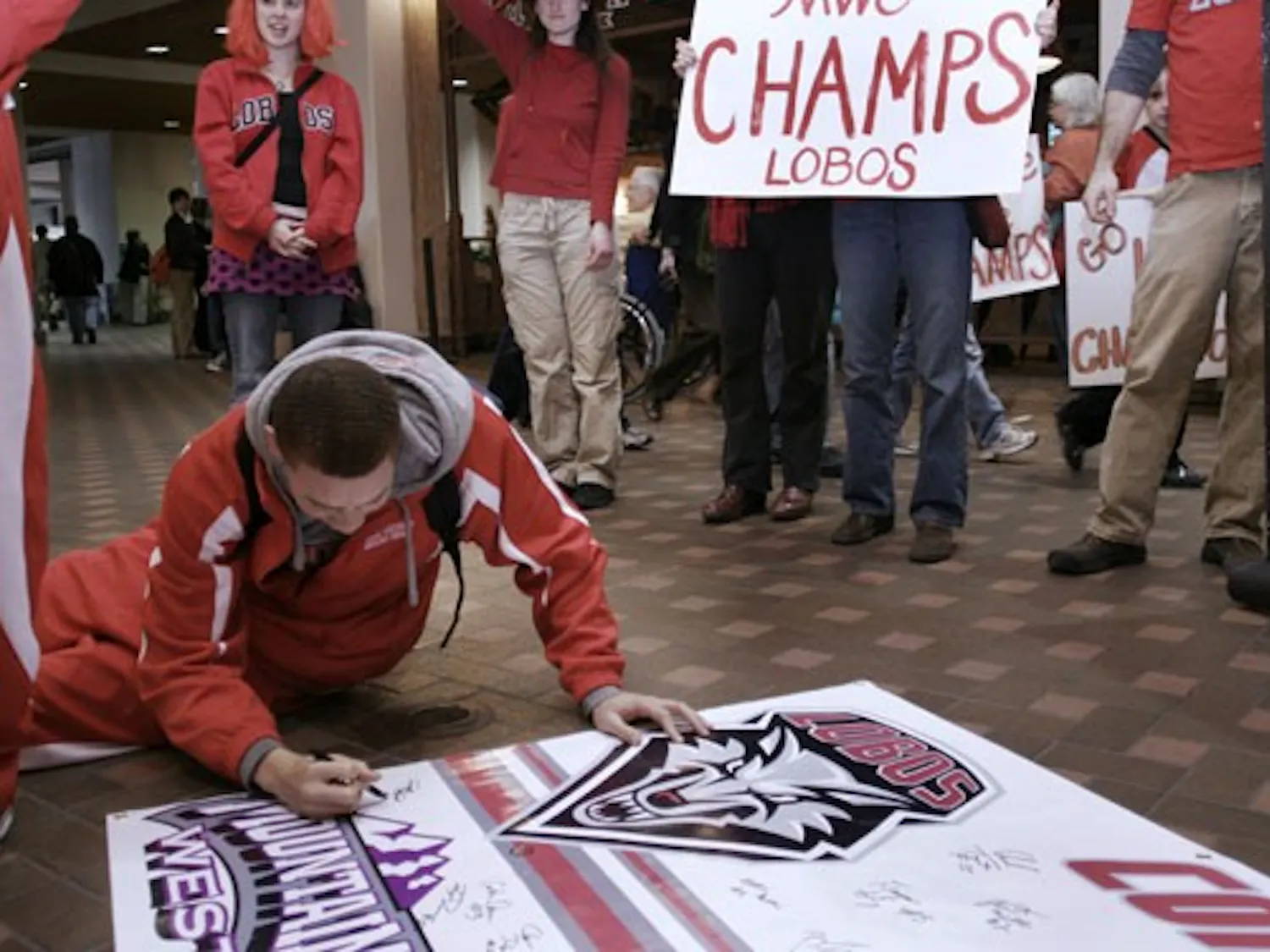 Phillip McDonald of the Lobo men's basketball team signs a poster at the Albuquerque International Sunport on Sunday after flying in from Wyoming. UNM fans packed the Sunport to welcome the Lobos, who beat the Cowboys at home Saturday to snag a share of t