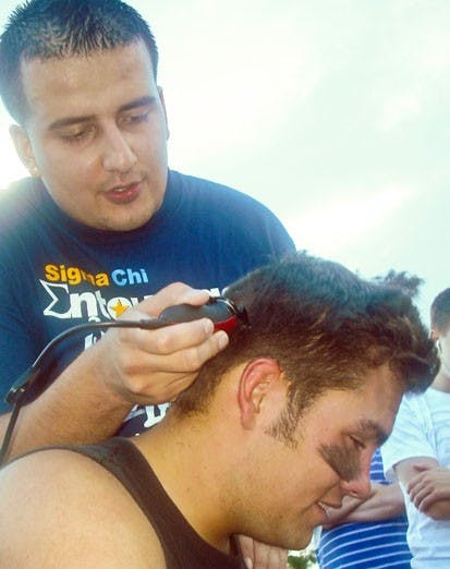 Mannie Gurule shaves fellow Sigma Chi fraternity member Jesse Varoz's head Saturday. The fraternity raised $268 for the Huntsman Cancer Institute when Varoz and Zach Taylor played a tennis match. Varoz lost.