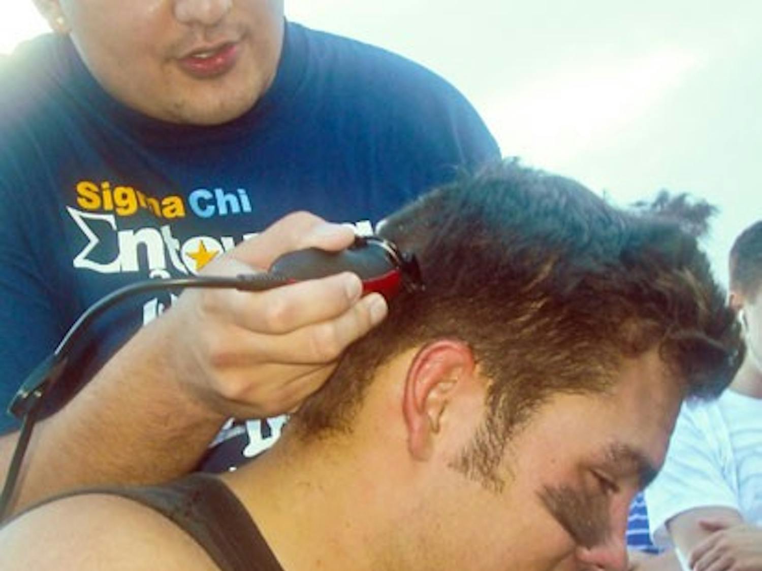 Mannie Gurule shaves fellow Sigma Chi fraternity member Jesse Varoz's head Saturday. The fraternity raised $268 for the Huntsman Cancer Institute when Varoz and Zach Taylor played a tennis match. Varoz lost.