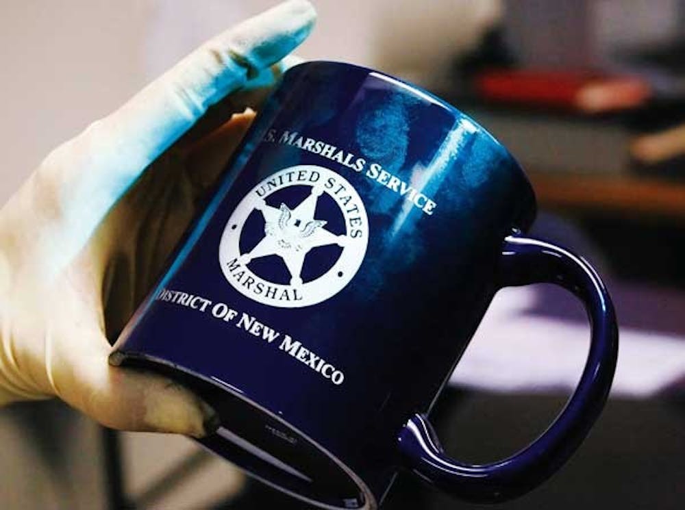 Detective Nina Fox uses a green light to show fingerprints on a coffee mug during a demonstration Tuesday at the UNM Police Department.