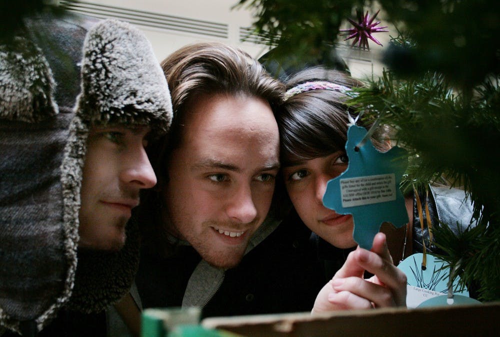 	Sophomore Tyler Mound, left, senior Simon Walker, center, and freshman Adeline Murthy read an ornament on the Giving Tree in the SUB atrium.  Each ornament describes a gift requested for a child or family in need. UNM community members can purchase the gifts and drop them off in the ASUNM office by Dec. 14.