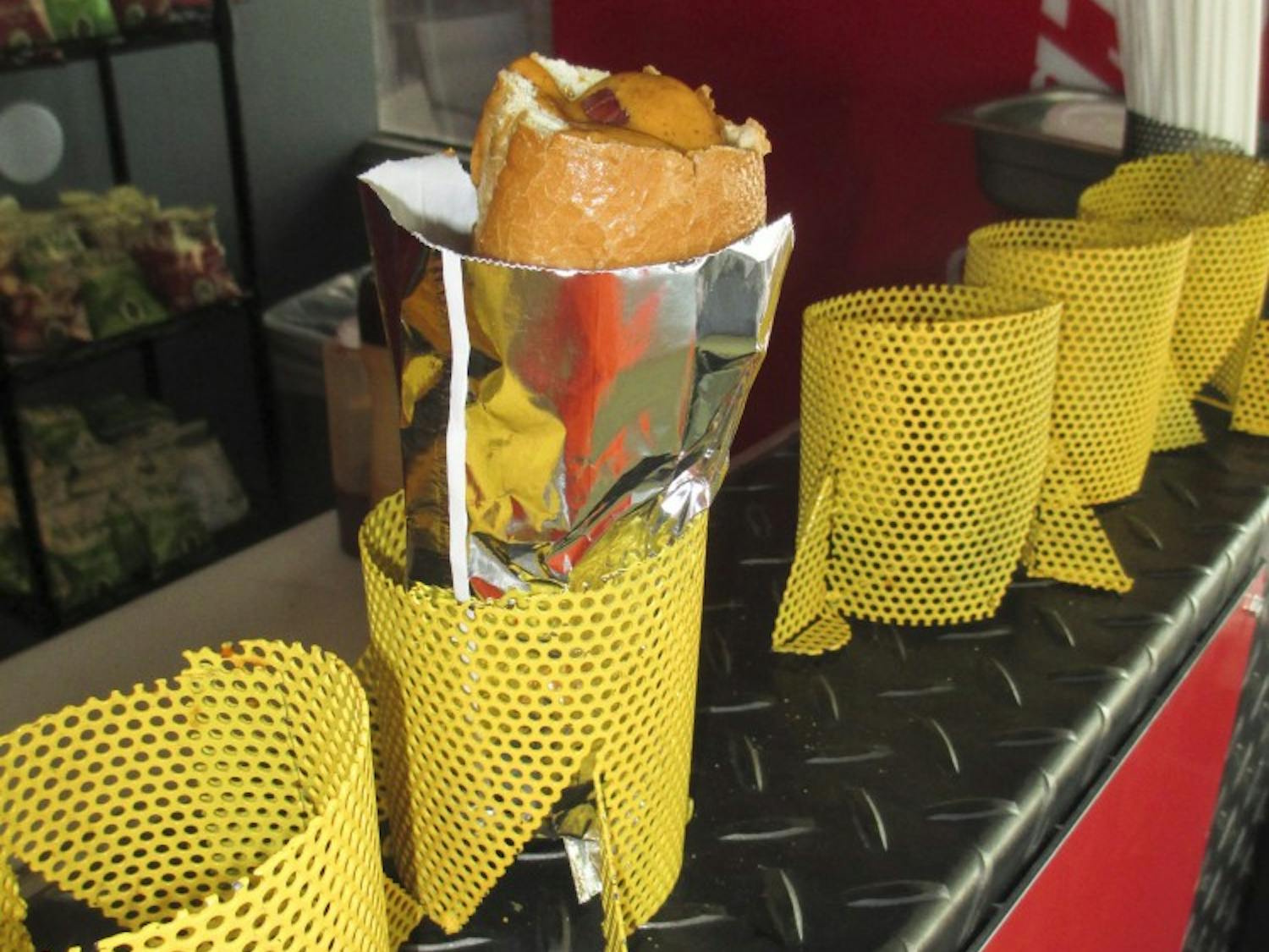 The finished Torpedo Dog, complete with red chile mustard in bread toasted from the inside, sits in a steel basket, ready for a customer.