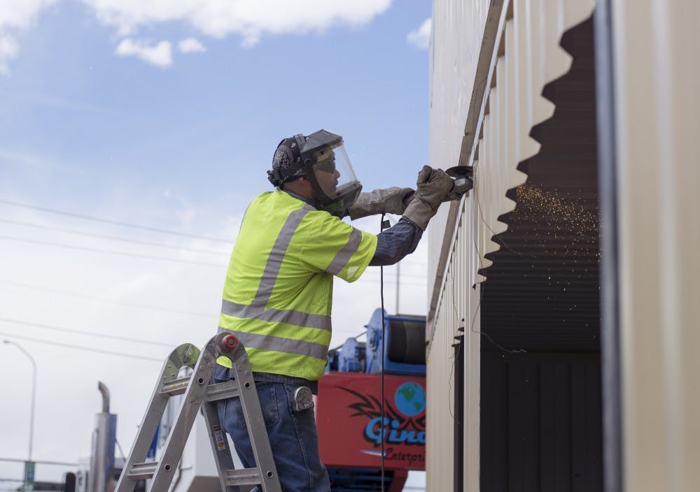 A worker uses his angle grinder to remove sections from a shipping container that will become a storefront for Green Jeans Farmery. Green Jeans Farmery, along with other local businesses, such as Amore Pizzeria and Santa Fe Brewing, will use recycled, retrofitted shipping containers as an eco-friendly alternative to traditional building structures. 