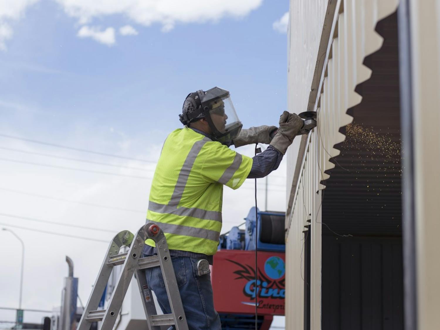 A worker uses his angle grinder to remove sections from a shipping container that will become a storefront for Green Jeans Farmery. Green Jeans Farmery, along with other local businesses, such as Amore Pizzeria and Santa Fe Brewing, will use recycled, retrofitted shipping containers as an eco-friendly alternative to traditional building structures.