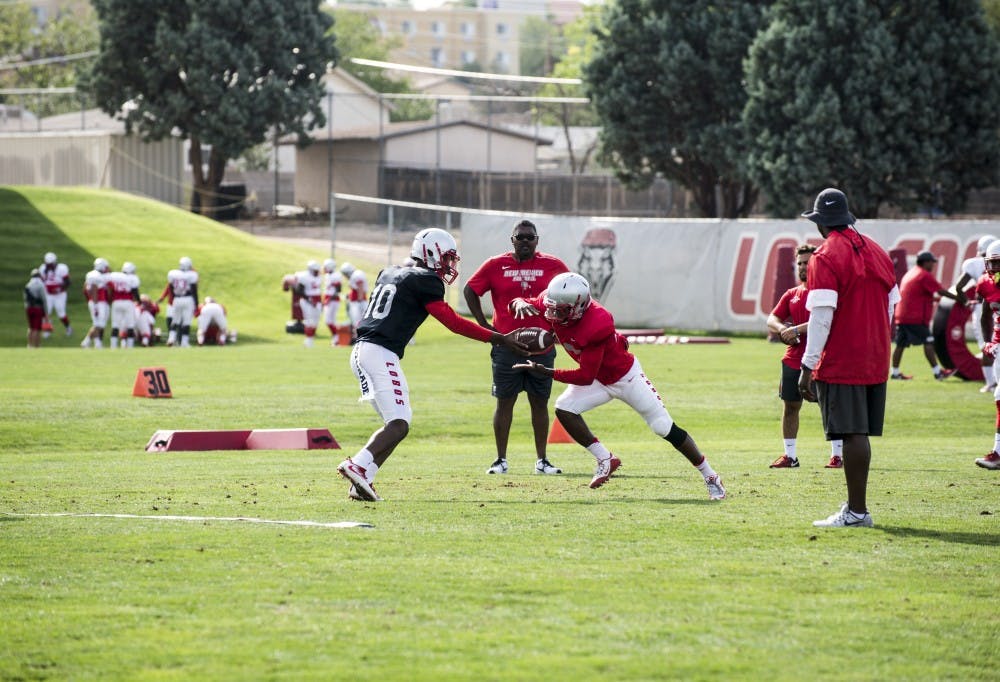 Quarterback Trae Hall hands the ball off to running back Tyrone Owens as offensive coordinator Calive Magee looks on during drills on August 21, 2018.