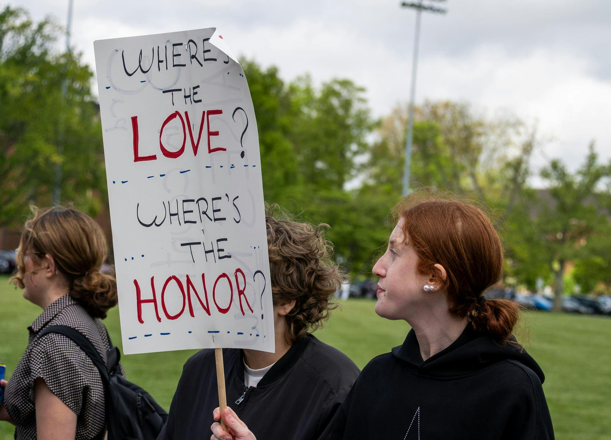 Student stands on Cook Field with a protest sign.