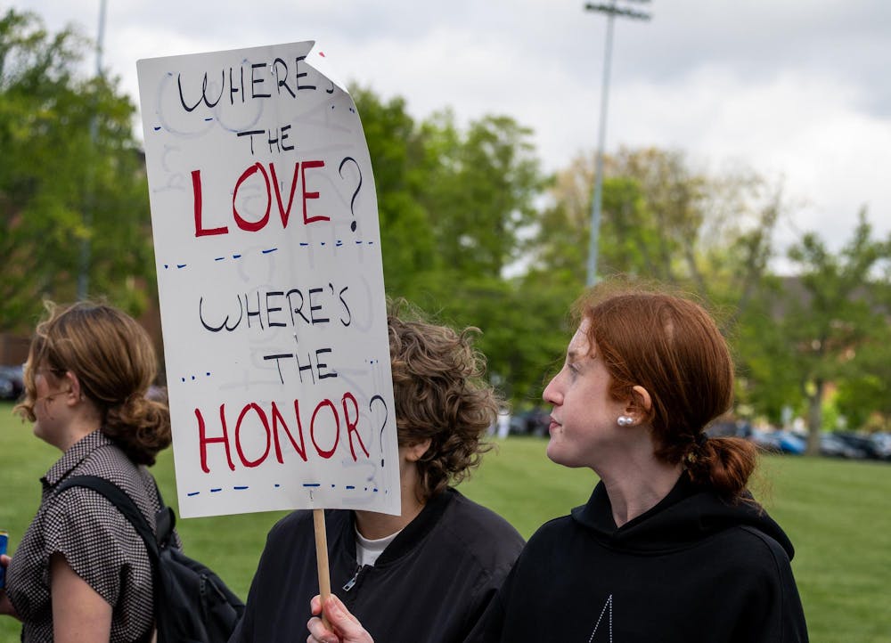 Student stands on Cook Field with a protest sign.