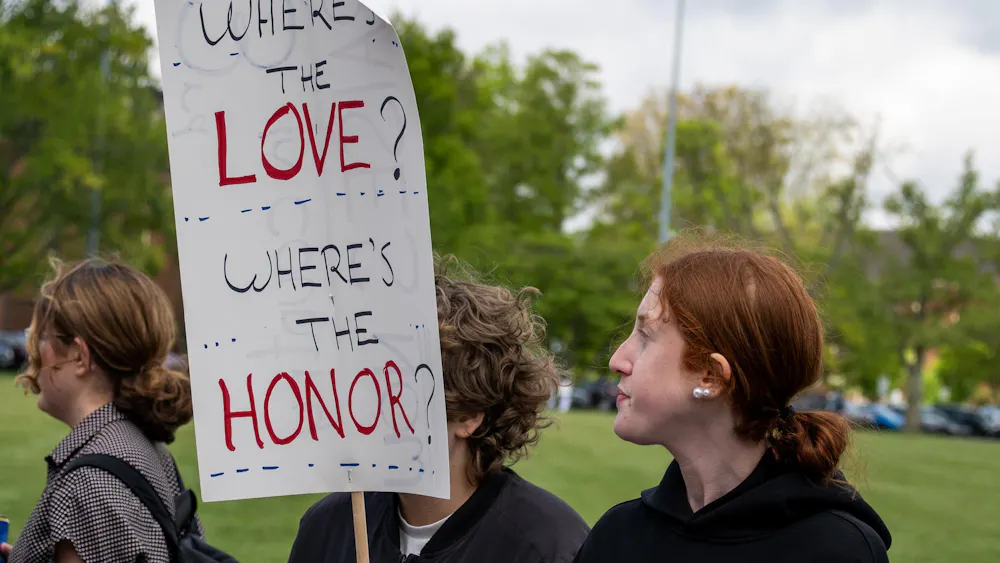 Student stands on Cook Field with a protest sign.