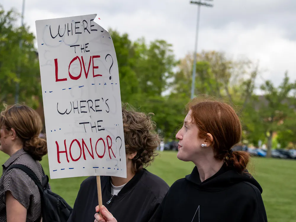 Student stands on Cook Field with a protest sign.