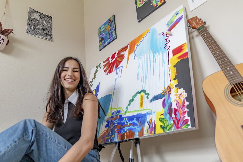 <p>Student artist Sophia Thompson turned to painting for comfort during the pandemic. Behind her is an unfinished piece.</p>