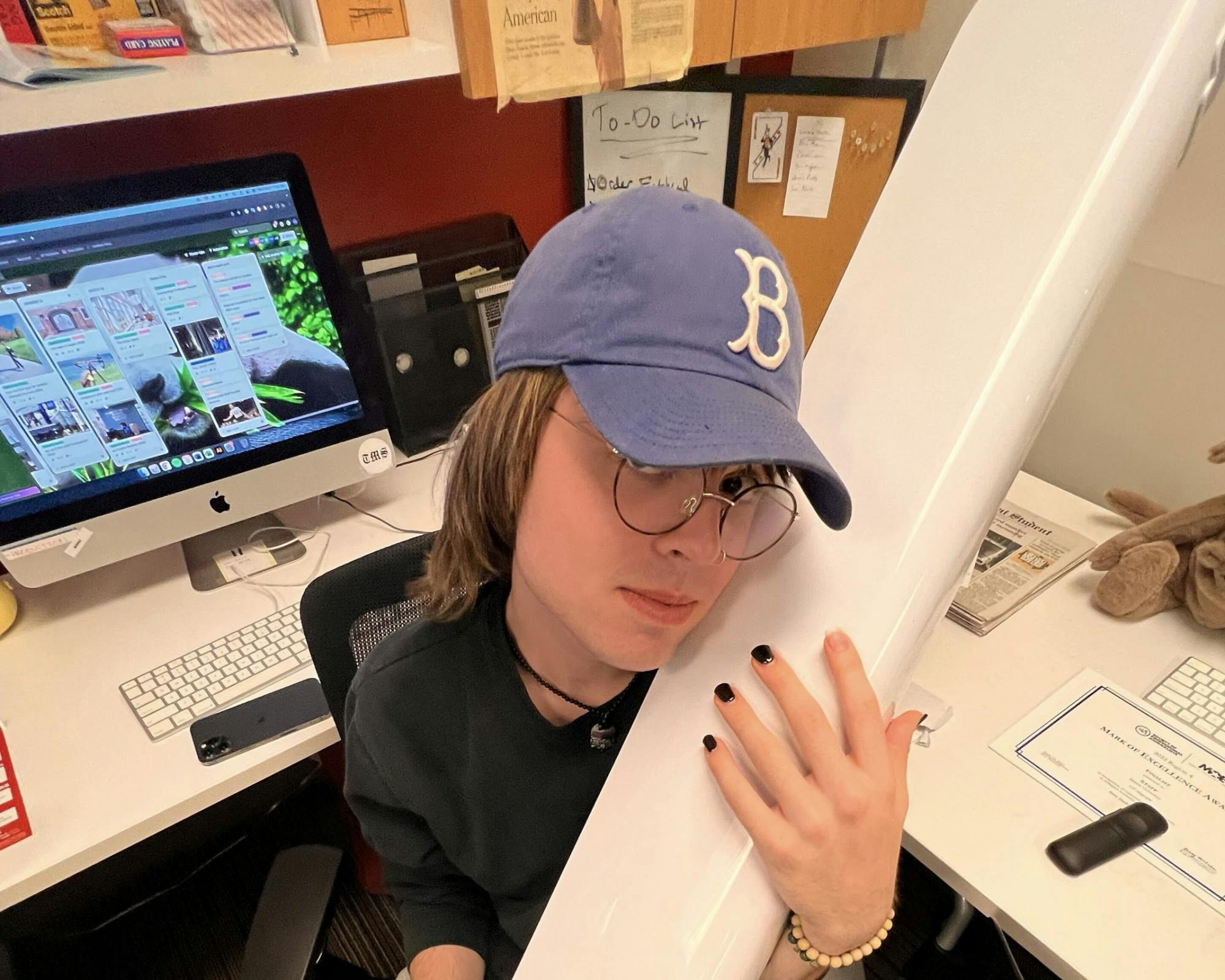 Devin Ankeney holding their dear and true love: the first newsroom fan while they sit in front of a whiteboard that has still not been erased a year later. 