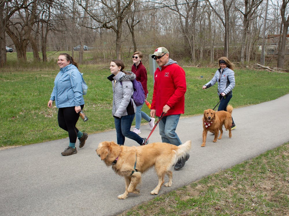 Alexandria Coffman (left) walks with Miami President Greg Crawford, his wife Renate, their two dogs Ivy (front) and Newton (back), and other students.