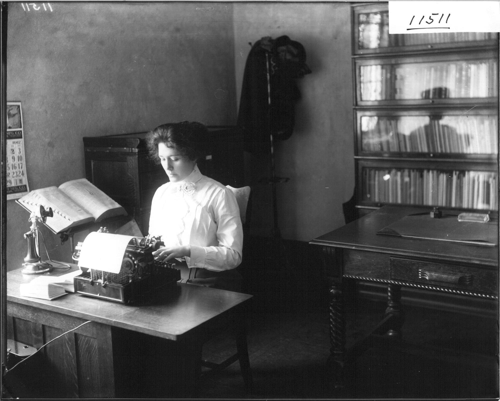 Secretary for the Dean of Education sits at a desk using a typewriter in 1912.