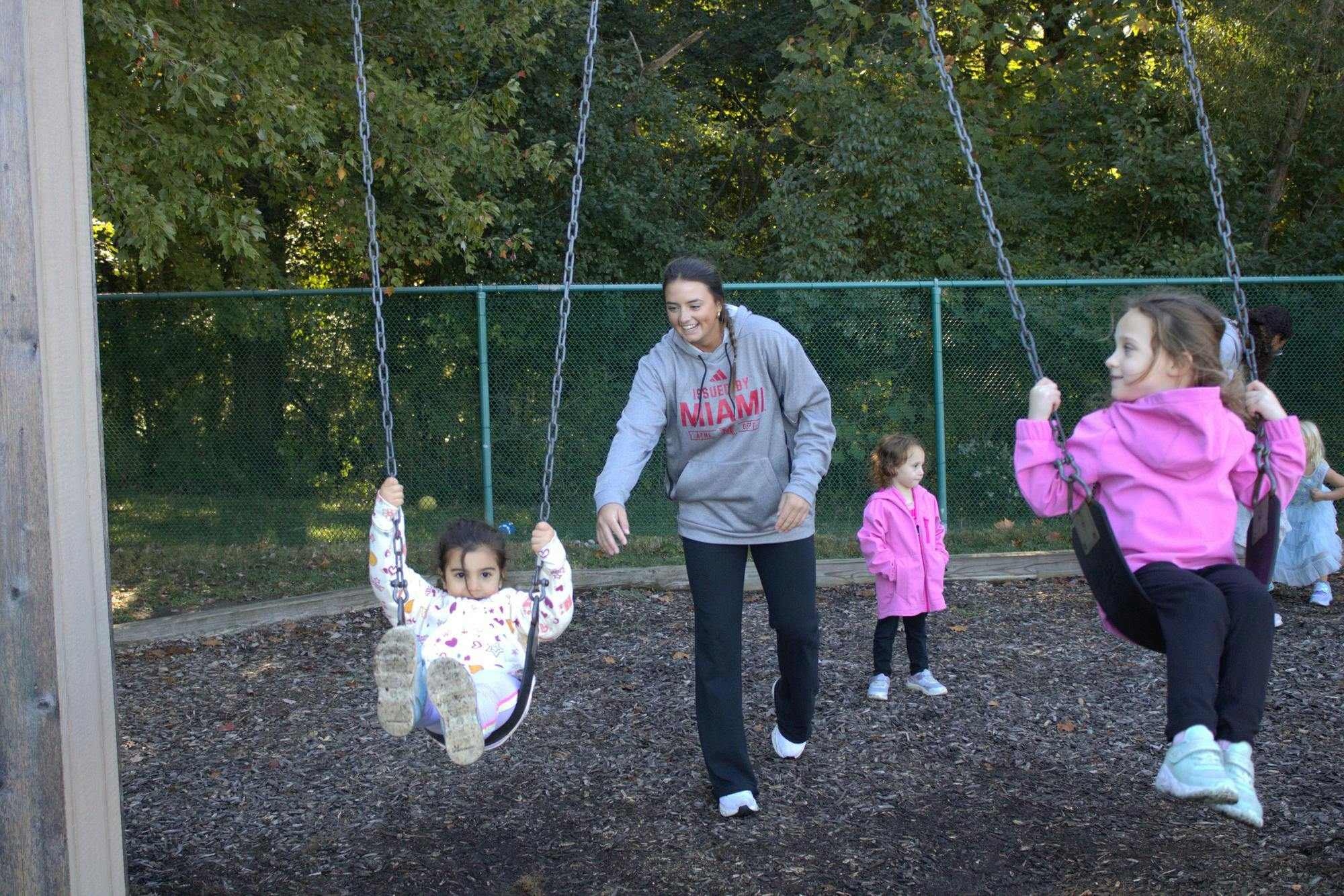 Softball player Leila Mathis pushes two kids on the swings at the Miami Child Development Center on Western campus.