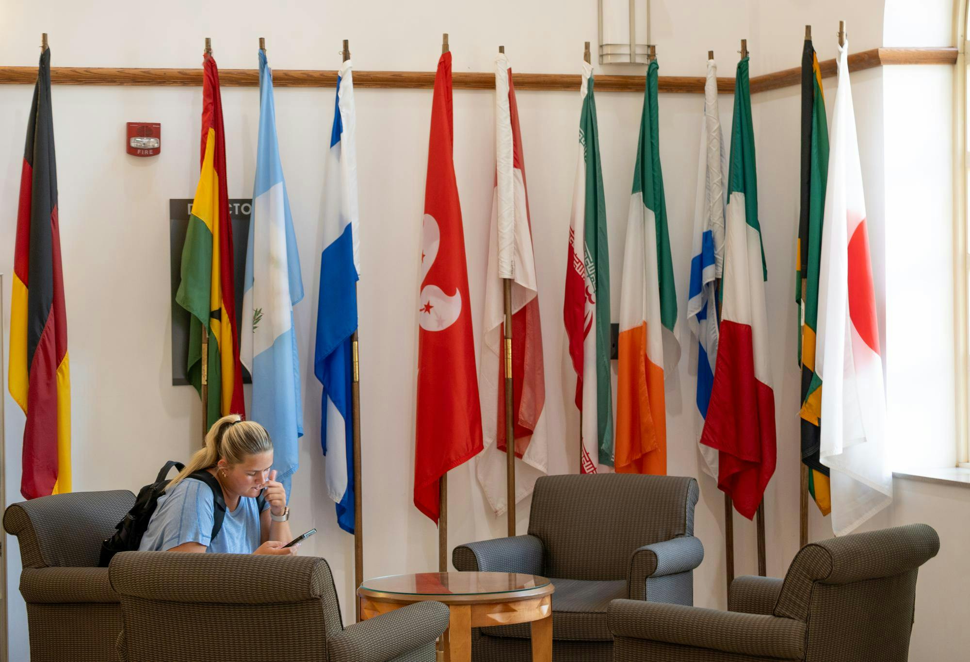 A student sits by the flags in MacMillan Hall, home to the International Student and Scholar Services.