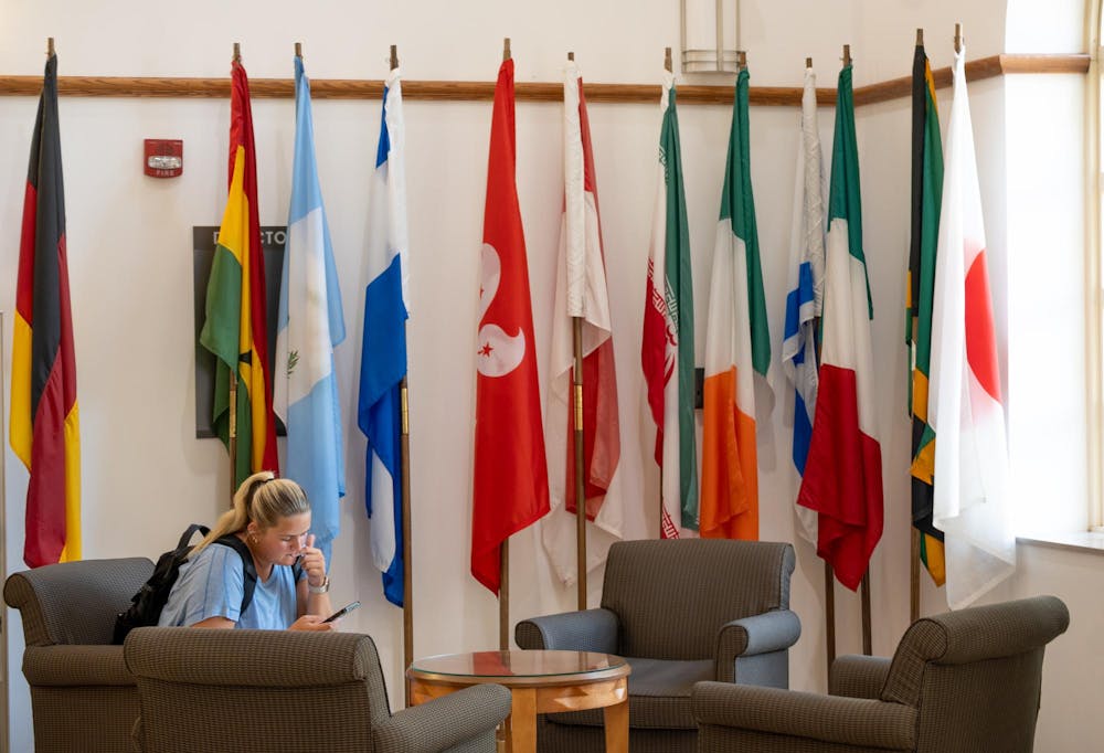 A student sits by the flags in MacMillan Hall, home to the International Student and Scholar Services.