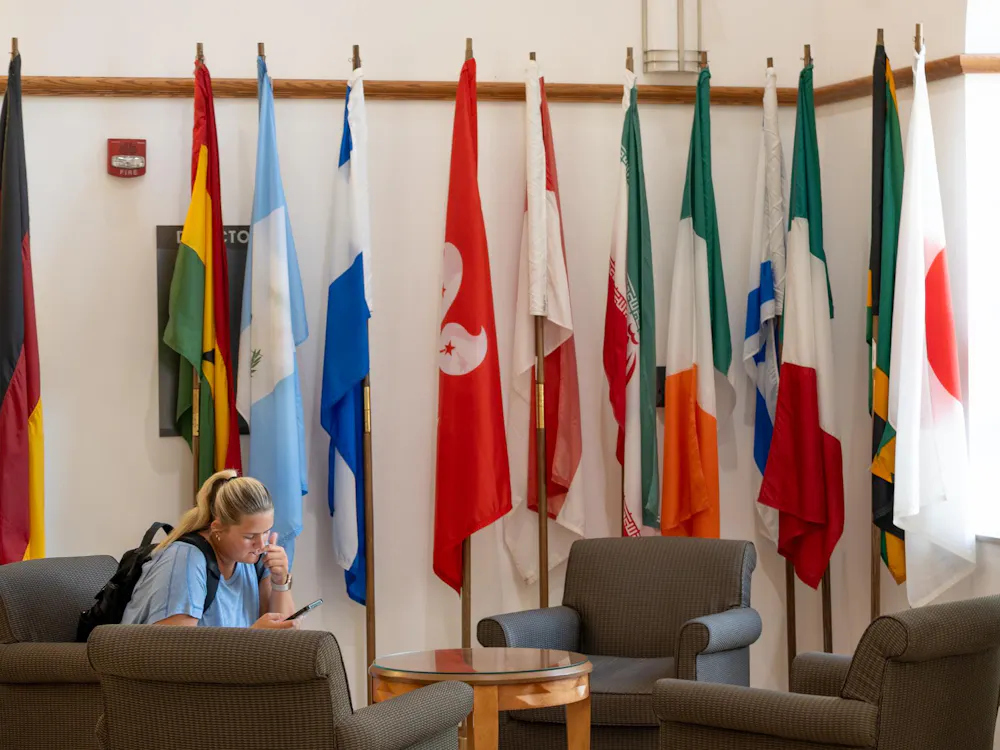 A student sits by the flags in MacMillan Hall, home to the International Student and Scholar Services.