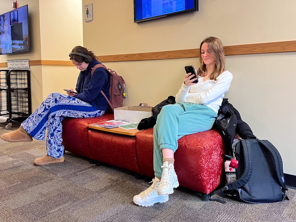 Two students scroll on their phones in-between classes in Williams Hall. 