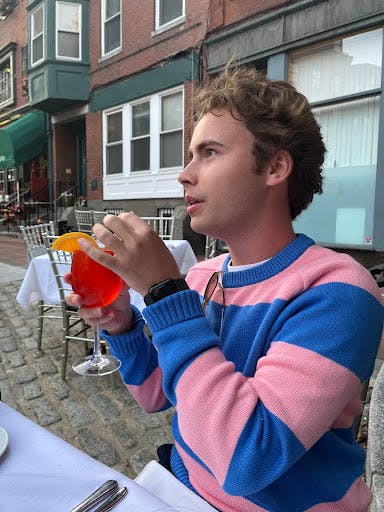 Morrison wears a pink and blue striped sweater from J.Crew while having an aperol spritz in downtown Boston.