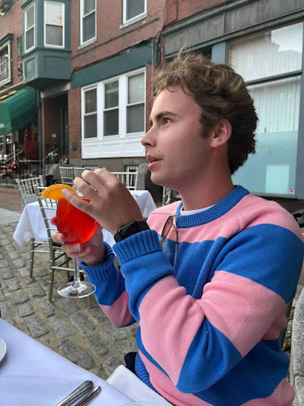 <p>Morrison wears a pink and blue striped sweater from J.Crew while having an aperol spritz in downtown Boston.</p>
