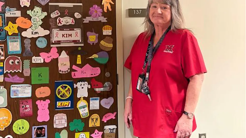 Building Grounds Associate Kimberly Durham in front of her supply closet, decorated by students and Resident Assistants in Hepburn Hall.
