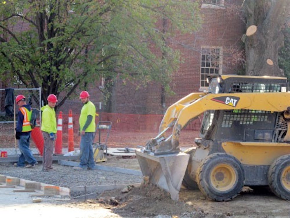 Construction workers look on as a Bobcat is used to help level a section of ground by Culler Hall.