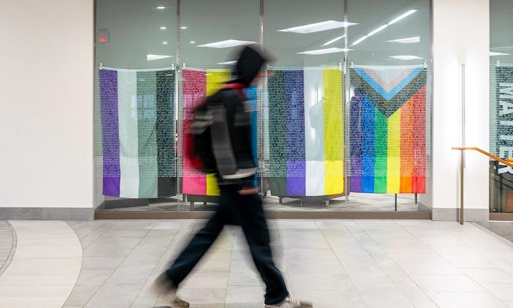 A student walks by an array of LGBTQ+ pride flags displayed in the former Center for Student Diversity and Inclusion