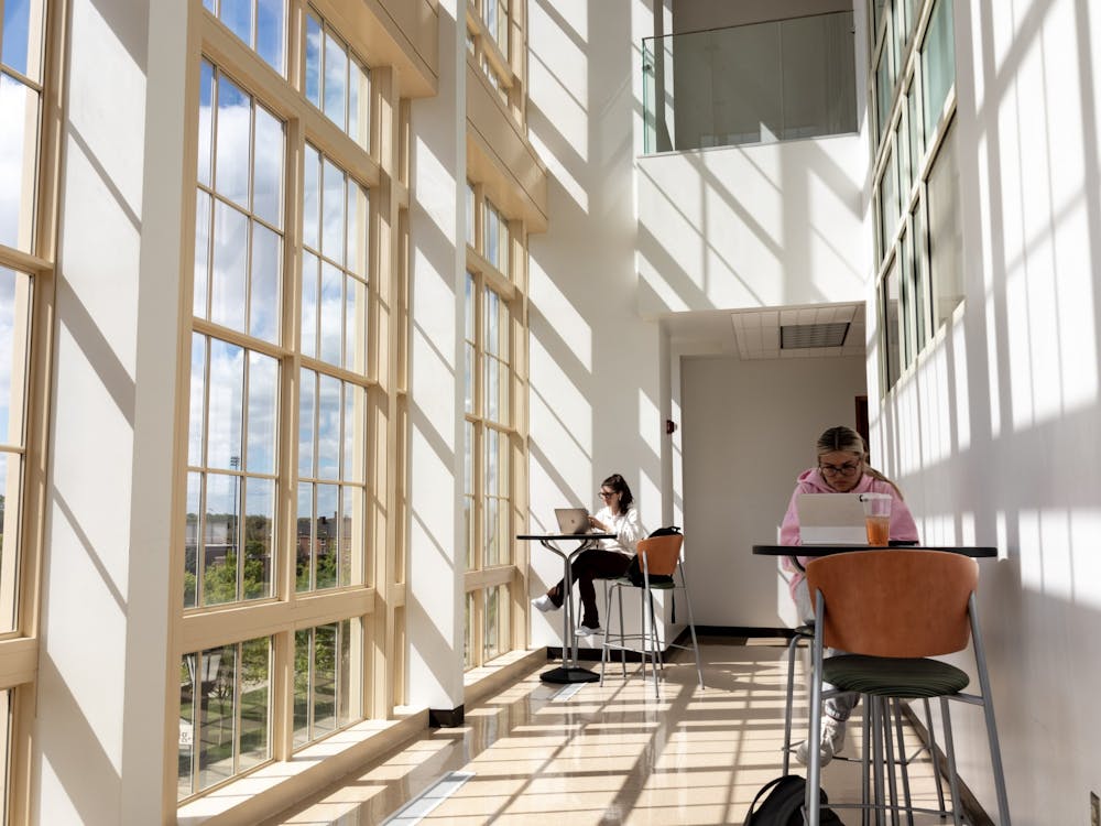 Two students study upstairs next to the two-story windows in the Psychology Building.