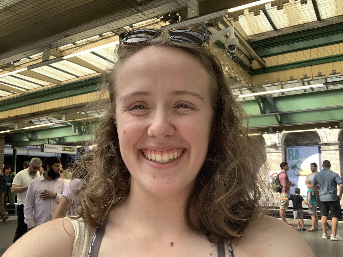 Abbey Elizondo, smiling as widely and glowingly as ever, stands in London at a train station.
