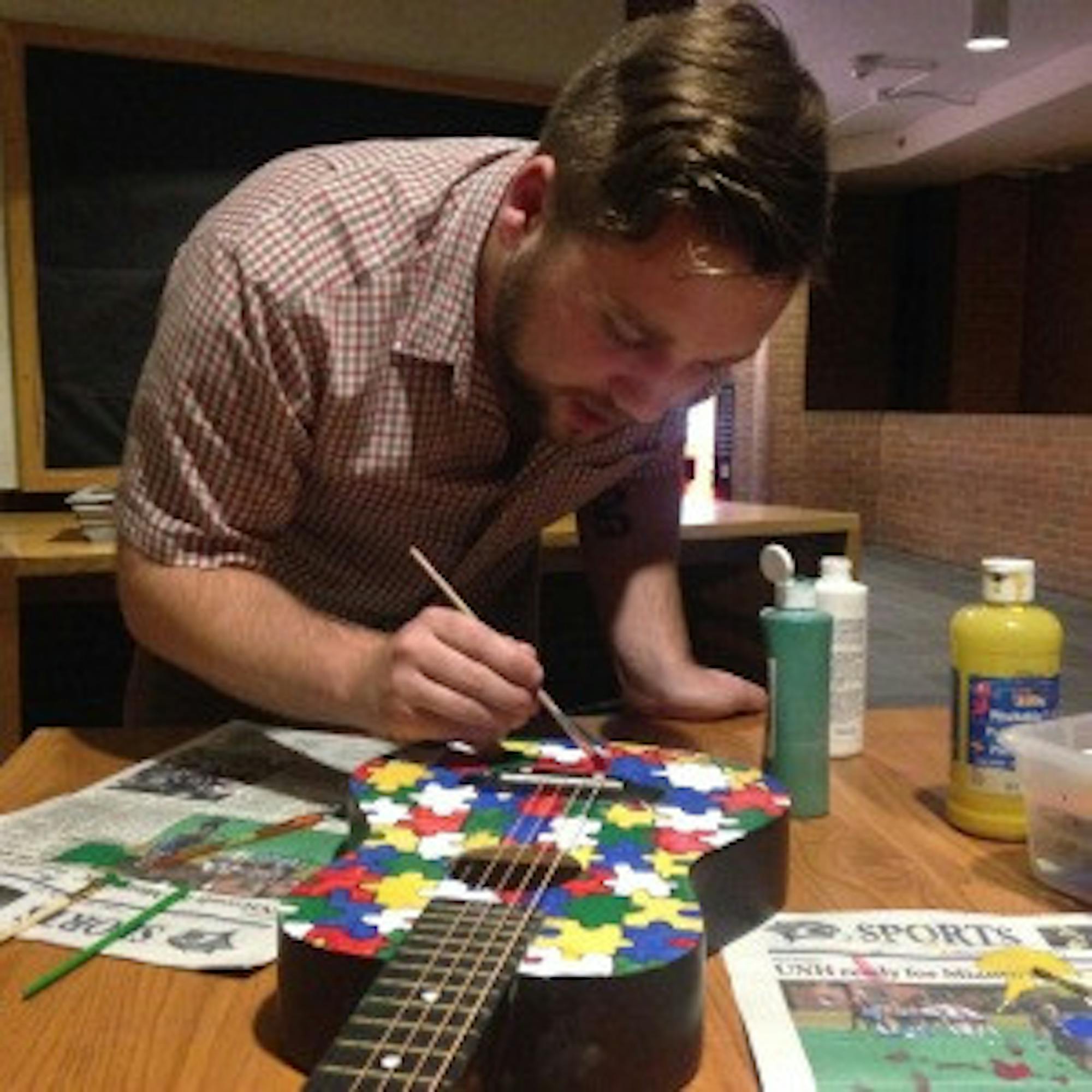 Melissa Proulx/staff Cody Waites diligently works on his art project, painting colorful puzzle pieces on a guitar. Waites is a multi-instrumentalist who enjoys helping children with disabilities through music therapy.