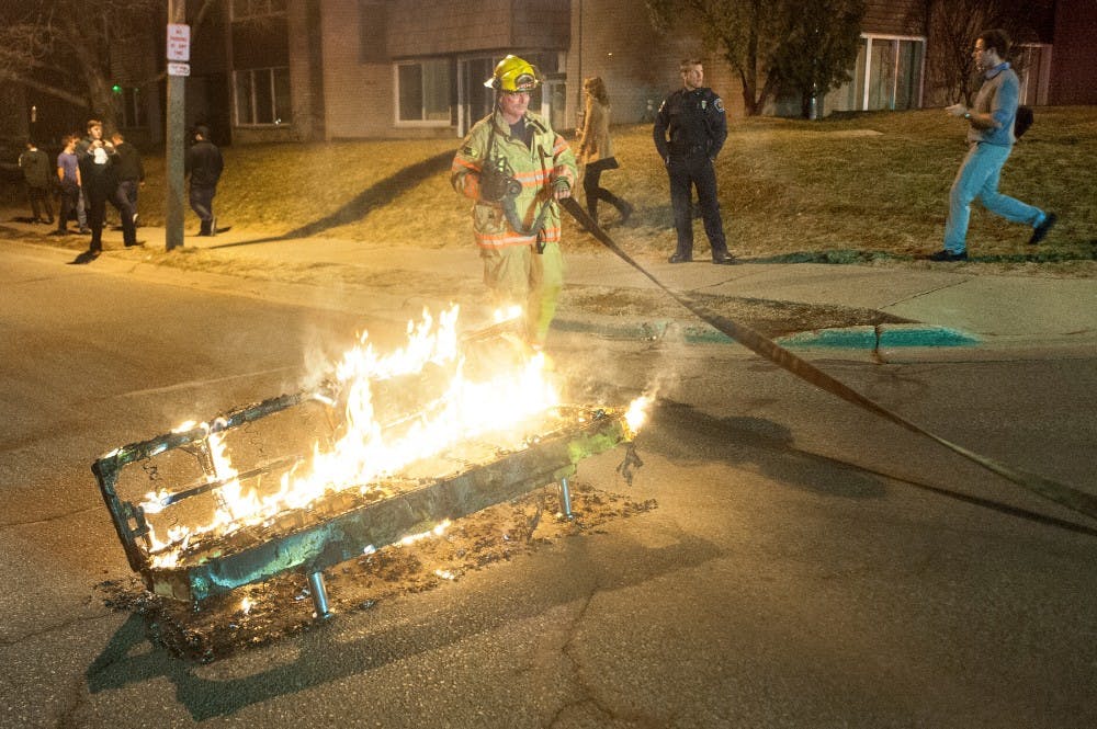<p>A fire fighter puts out a couch fire in the intersection of River St. and Victor St. in Cedar Village during the early hours of Saturday, March. 30, 2013, after the men's basketball team lost to Duke in the fourth round of the NCAA tournament. The East Lansing Police Department responded to over 14 fire disturbances on Saturday morning. The State News</p>