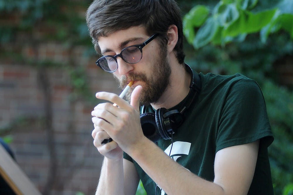 <p>Computer science senior Daniel Roman smokes a cigarette on Sept. 29, 2014, outside of Wells Hall. The smoking policy requires students to not smoke within 25 feet of the doors of buildings on campus. Aerika Williams/The State News</p>