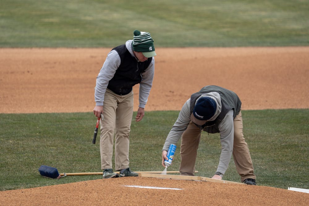 <p>The MSU grounds crew paints the Spartan helmet on the back of the pitcher's mound in preparation for Michigan State's home opener against Western Michigan, on March 22, 2023.</p>