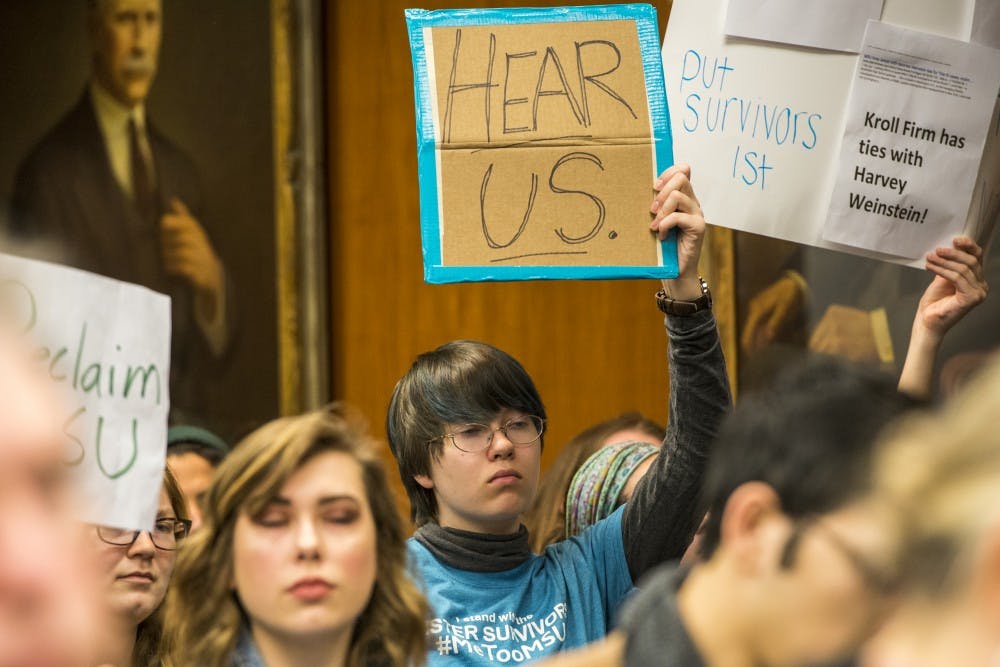 Protesters from Reclaim MSU hold signs during the Board of Trustees meeting on Feb. 16, 2018 at the Hannah Administration Building. (Nic Antaya | The State News)