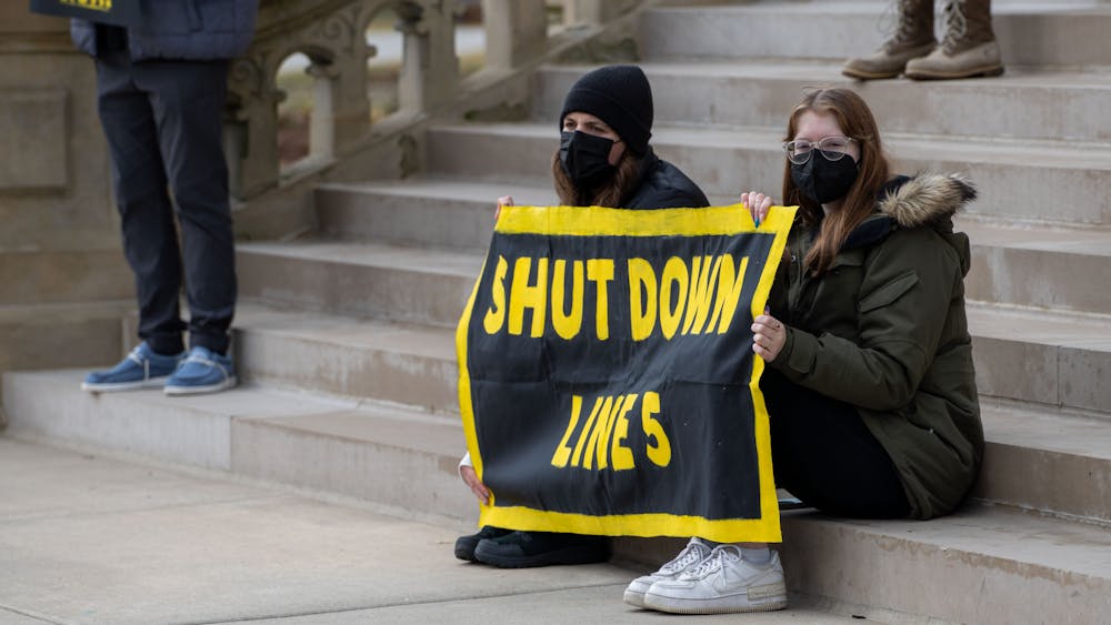 Two Michigan State University students sit on the capitol steps holding a "Shut Down Line 5" sign during the Friday for Futures Event in Lansing on March 25th, 2022.