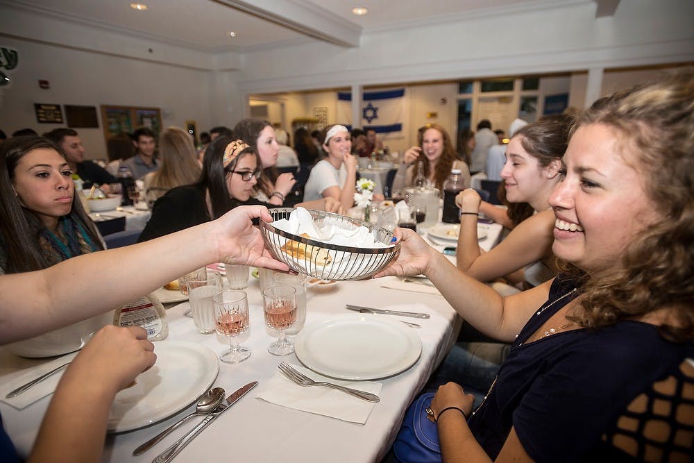 <p>Psychology freshman Jane Fox, right, takes a bread basket from Lyman Briggs sophomore Hayley Siegel on Sept. 24, 2014, at a Rosh Hashana dinner at the Lester and Jewell Morris Hillel Jewish Student Center, 360 Charles St. Rosh Hashana is the Jewish New Year and was celebrated by students with services before the dinner. Erin Hampton/The State News</p>