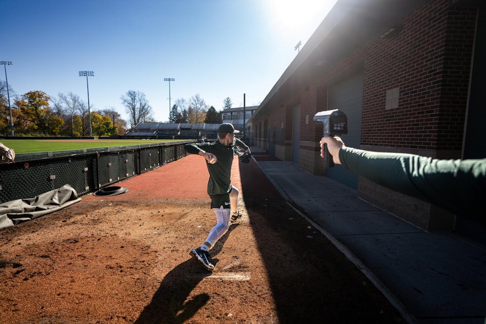 Michigan State redshirt junior right-handed pitcher Ryan Szczepaniak (42) pitches in the bullpen during pitching practice at McLane Stadium on Nov. 7, 2024. MSU sophomore right-handed pitcher Gavin Moczydlowsky (22) tracks the speed of the pitch using a radar gun.