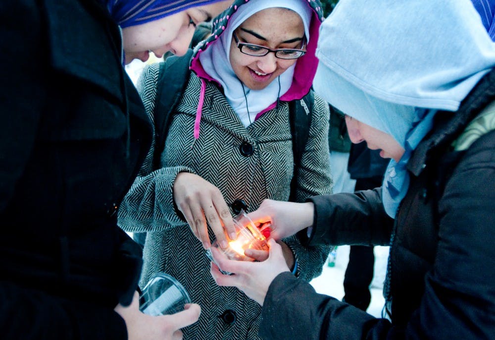No-preference freshman Sarah Mahmoud, left, huddles with psychology sophomore Essra Abdel-Azim, center, and chemical engineering senior Sara Saleh, right, as they try to keep the wind from blowing out their candles. Amnesty International MSU and the Muslim Student Association held a vigil on Wednesday night at the rock on Farm Lane to show support for the protests that have been sweeping across the Middle East and North Africa in recent weeks. Josh Radtke/The State News