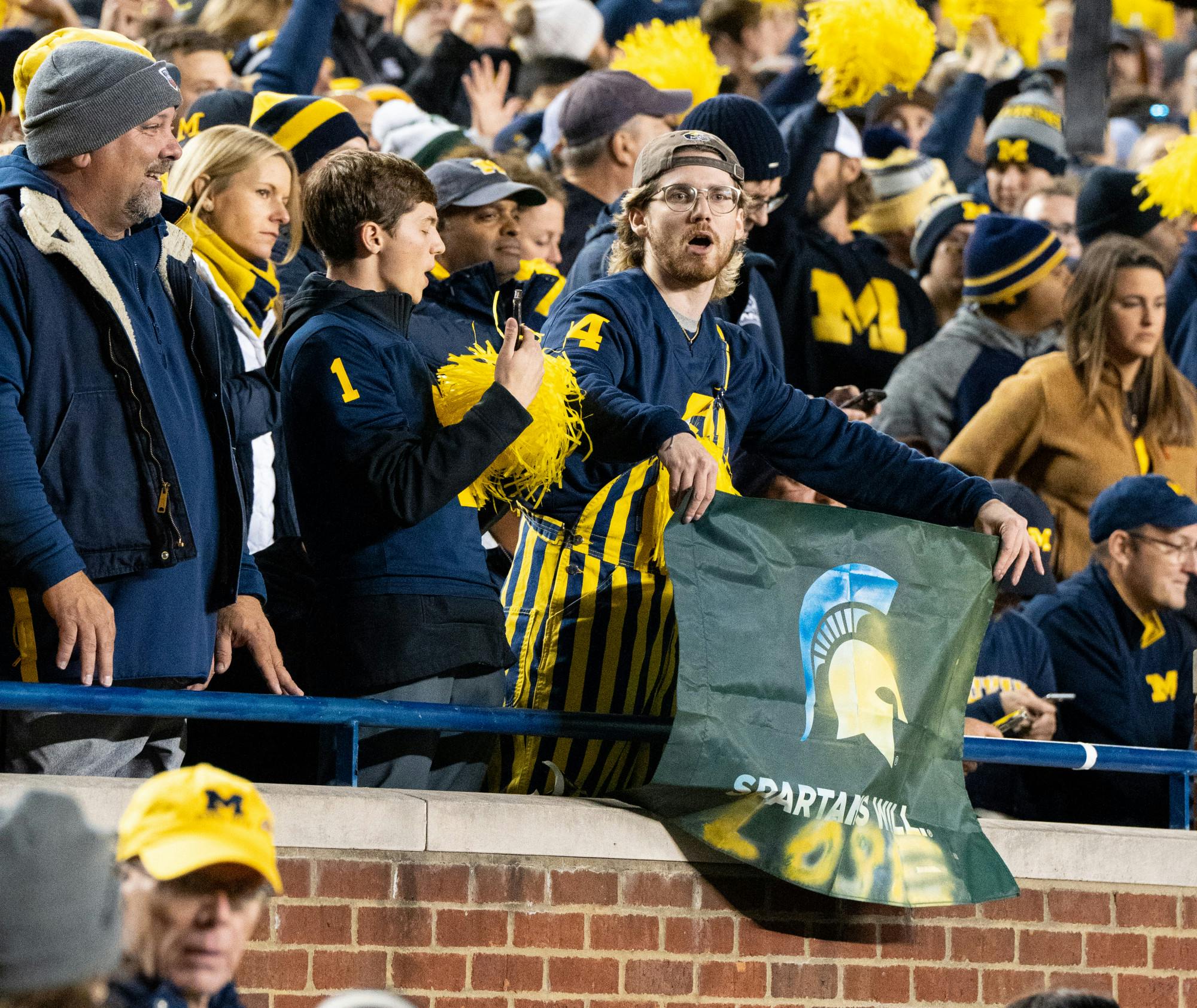 <p>A Michigan fan holds a flag painted blue and yellow that says "Spartans Will. LOSE". Spartans lost 29-7 to the Wolverines on Oct. 29, 2022.</p>