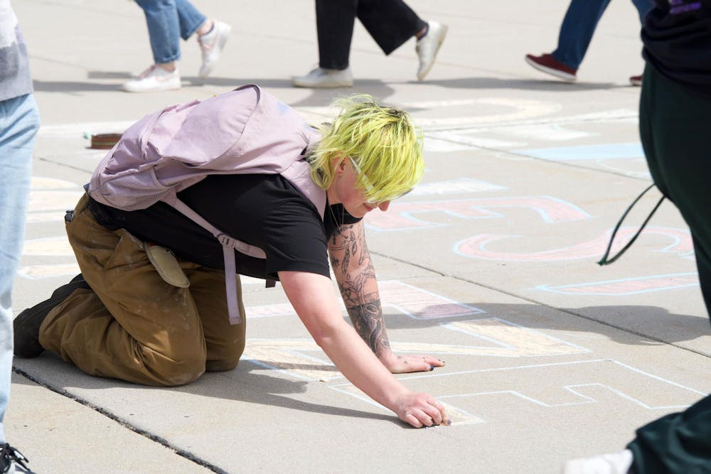 A protestor writes "denounce" and "divest" on the pavement outside the MSU Breslin Center on April 26, 2024. Protestors called on MSU to divest from Israel. 
