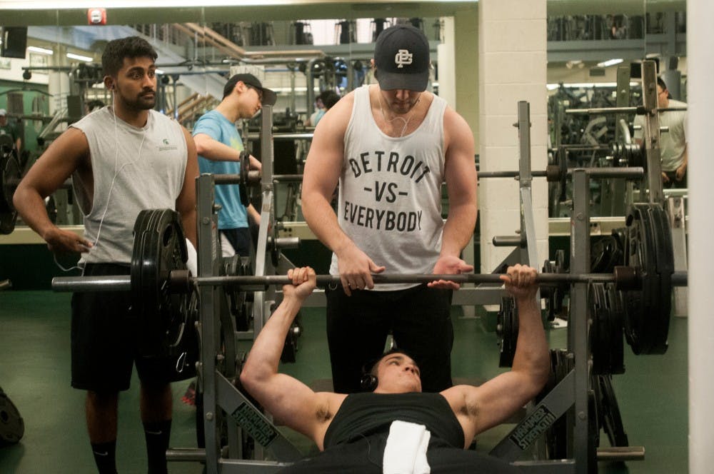 Nutritional sciences senior Ashwin Easow watches as human biology senior David Cook helps lift the bar for human biology senior Alex Parker at IM Sports-West on Jan. 8, 2016. Many students enter the new year by increasing visits to the gym. 