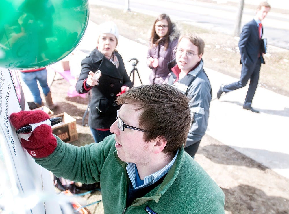 	<p>Jay Gage, president of the Student Association of Michigan, writes the finishing touches on the student debt board as group members watch Friday, March 22, 2013, at the rock on Farm Lane. The Student Association of Michigan held the event to raise awareness for the ongoing problem with student debt. </p>