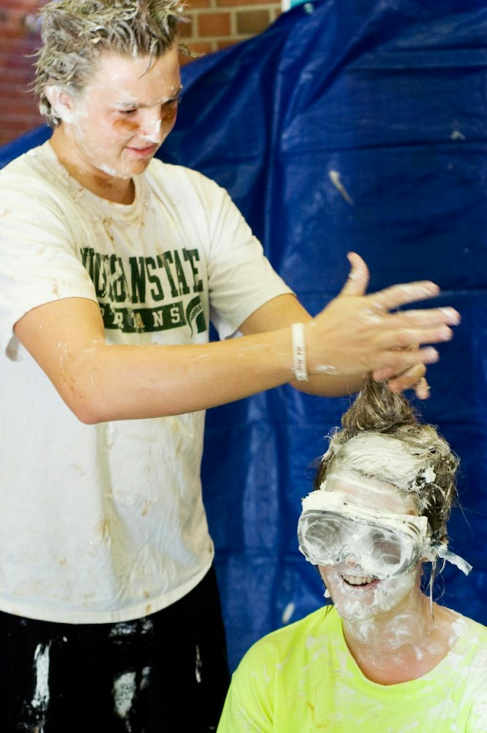 Social relations and policy sophomore Kevin O'Brien styles the whipped-cream-and-pudding-laden hair of child development sophomore Meghan Rohen at the Pie Your Mentor event held Tuesday at Case Hall. The money with which students purchased pies to throw at their mentors will go toward relief efforts in Japan. Marina Csomor/The State News