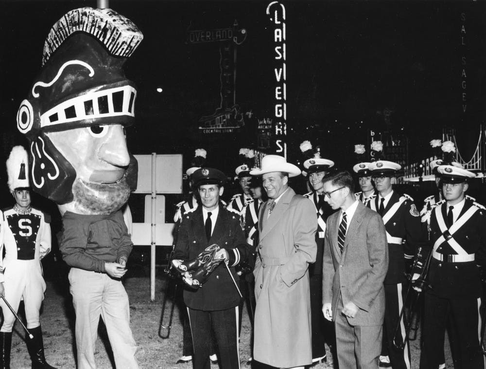 <p>Sparty’s  first look took the form of a massive paper mache head worn on a man’s  shoulders, a common look for mascots at the time. The mascot first made  its debut in the 1954 Rose Bowl parade, and the first head measured  about six feet tall. The original head is believed to have been made by  fraternity Theta Xi and was supposedly stolen during a MSU vs.  University of Michigan game and burned in 1955. </p><p>This picture features an early Sparty with former MSU Director of Bands Leonard Falcone, leading the marching band during a trip to the Rose Bowl in 1956.</p>