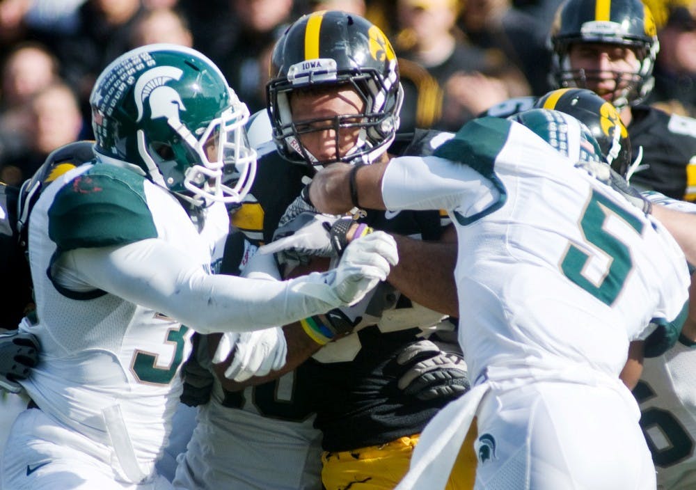 Senior safety Trenton Robinson, left, and junior cornerback Johnny Adams wrap up Iowa running back Marcus Coker Saturday at Kinnick Stadium in Iowa City, Iowa. The Spartans defeated the Hawkeyes 37-21. Matt Radick/The State News