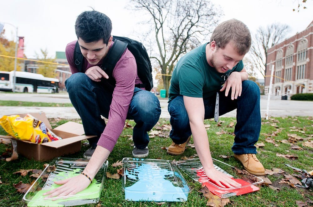 Chemical engineering seniors Evan Muller, left, and Jake Hoppert place their hands in paint to raise awareness about hazing on Tuesday, Oct. 23, 2012, at the rock on Farm Lane. The Panhellenic Council hosted the Hazing Prevention Week Banner Signing to bring awareness to hazing issues. Julia Nagy/The State News