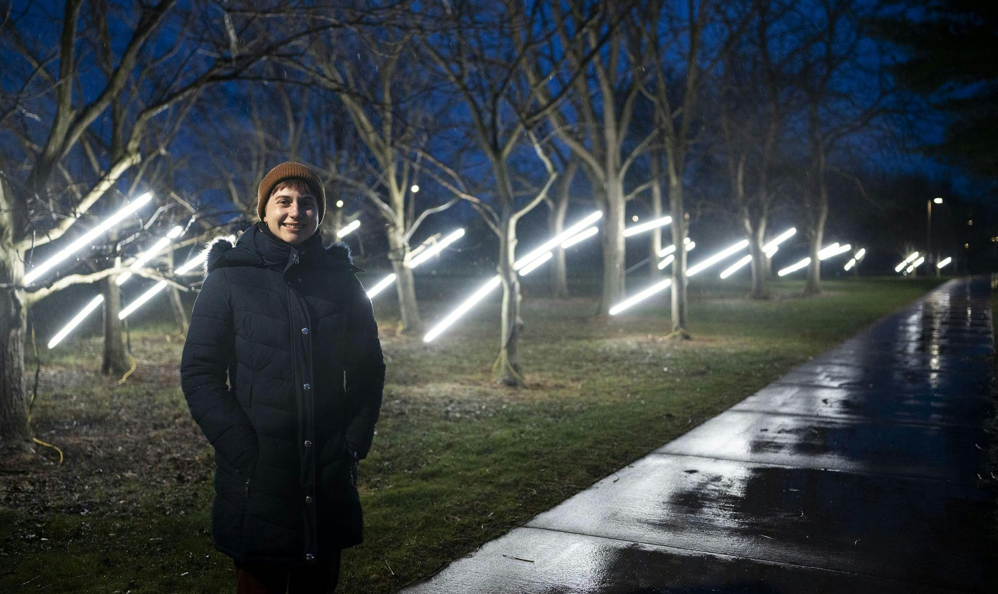 <p>MSU graduate student Hailey Becker stands at her art installation outside of Holden Hall on April 9, 2025. Becker's installation featured beams of light coming out of trees scheduled to be cut down for upcoming construction. She hoped this project will bring awareness to ecological grief. According to her artist statement, “the act of piercing the tree with light is a death ritual in which the community is given an opportunity to pay their respects to the trees, mitigating the shock of their imminent removal.”</p>