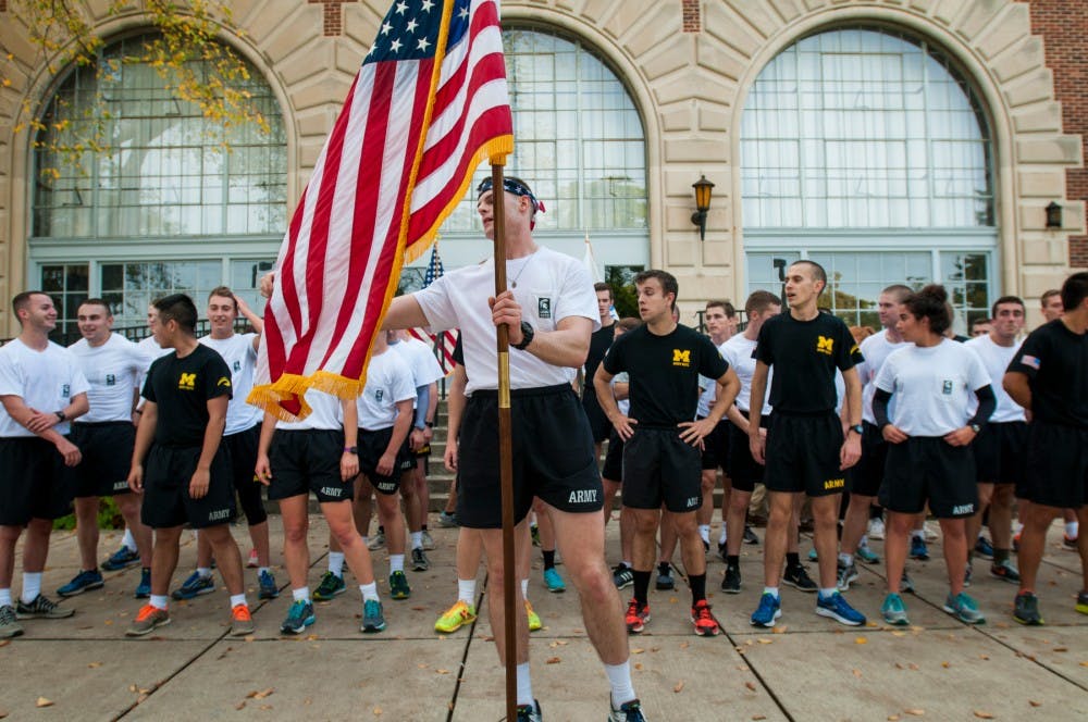 Business management junior Michael Stass adjusts the American flag while MSU and University of Michigan ROTC cadets stand behind him after finishing Alex's Great State Race on Oct. 28, 2016 outside of Demonstration Hall. MSU and U-M ROTC cadets joined together to run 64 miles from U-M's campus to MSU's campus while passing the game balls between cadets to honor Alex Powell, an MSU freshman who died in 2011.