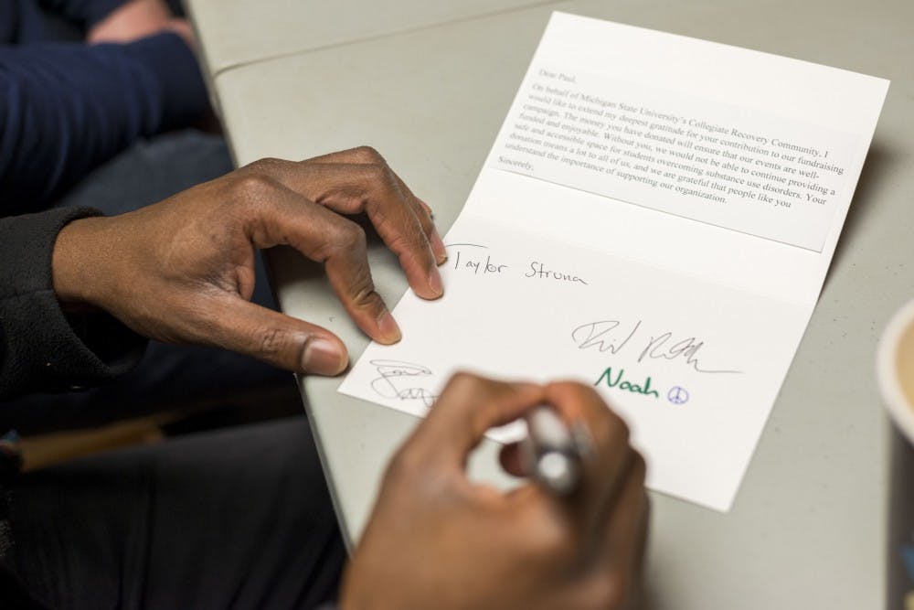 Business administration junior Josh Oyetubo signs a card during the MSU Traveler's Club meeting on March 31, 2017 at Olin Health Center. Members of the club signed cards that were then sent to club donors. The funds that the club receives are put towards the lounge space and events that are held by the club. The MSU Traveler's Club is a club that provides a social space and support for people who are in recovery from addiction. 
